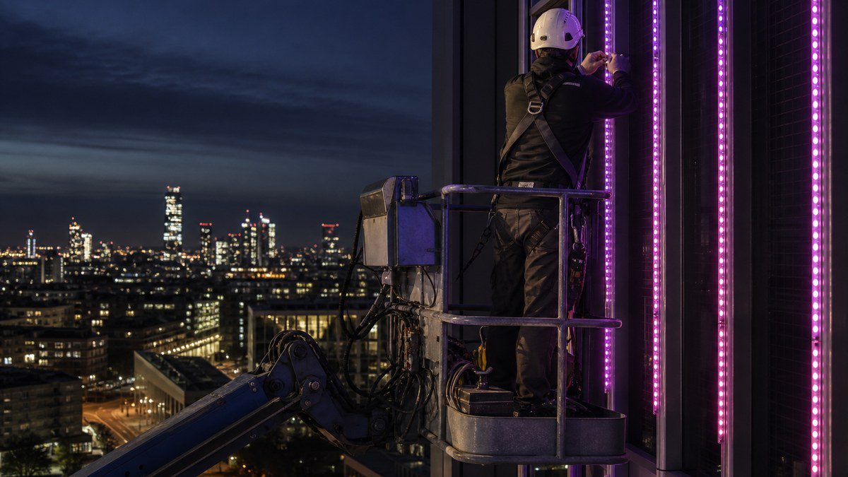 Lighting technician on a boom lift installing addressable LED pixel bars on a building facade at dusk
